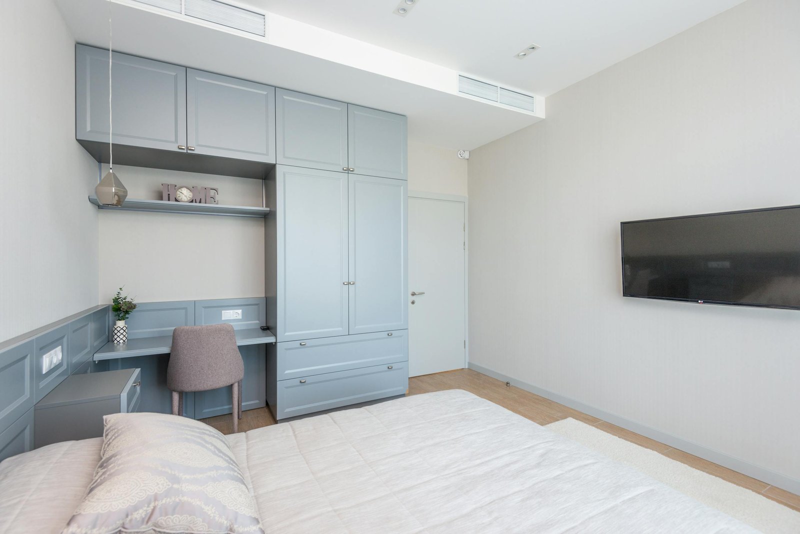 Bright minimalist bedroom with blue wardrobe and wall-mounted TV.