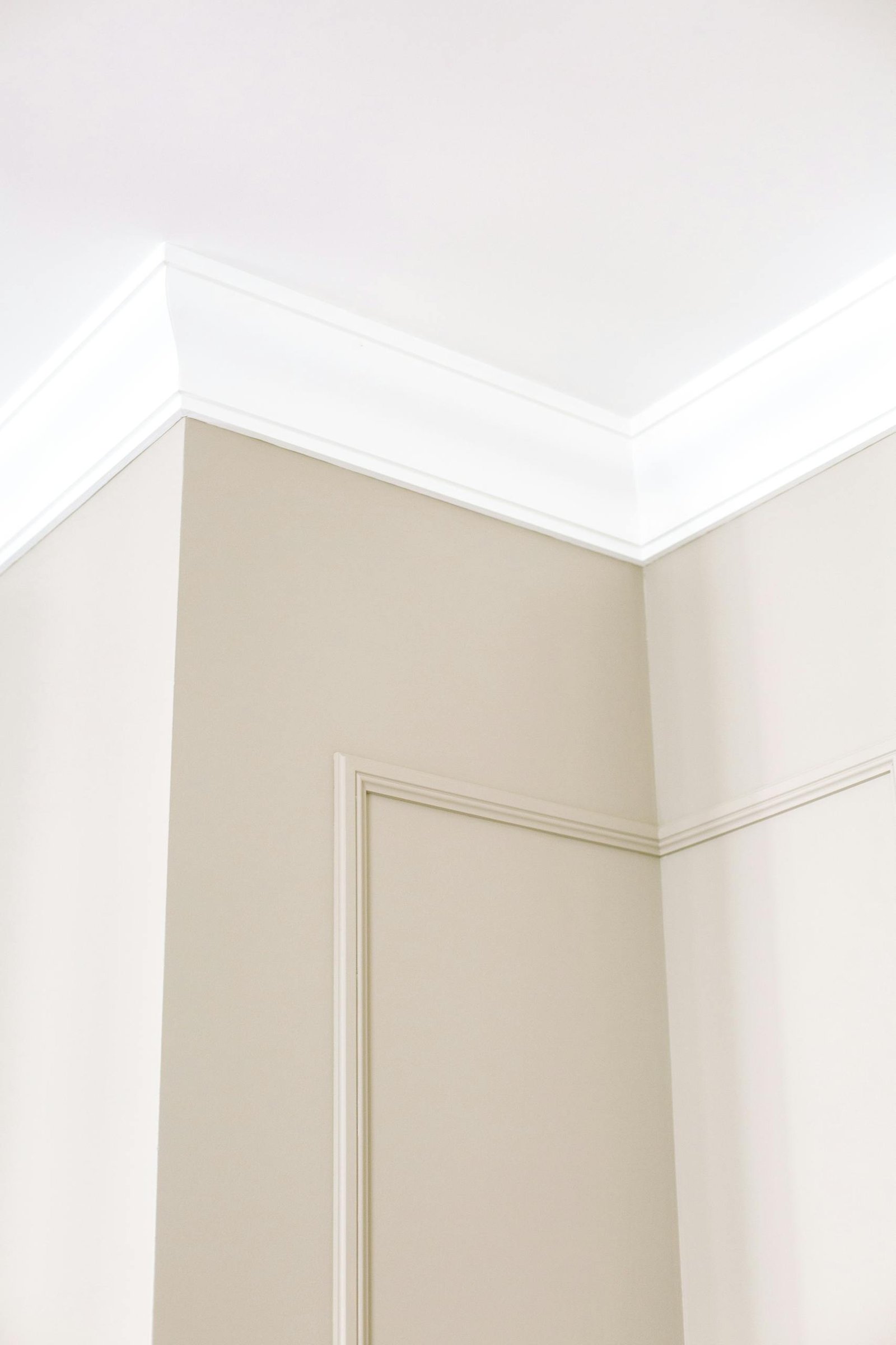 Close-up of intricate ceiling moulding and beige walls with minimalist design, showcasing home renovation details.